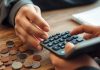 Person calculating savings interest with coins and calculator.